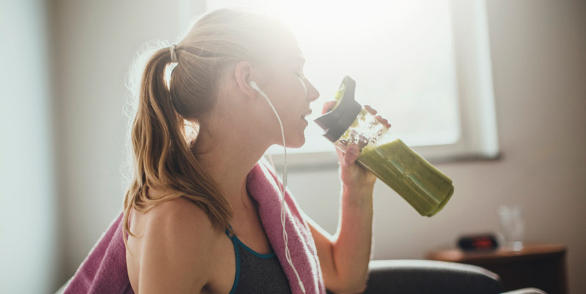 Mulher segurando uma garrafa com suco verde dentro