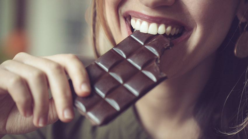 Mulher com barra de chocolate na boca