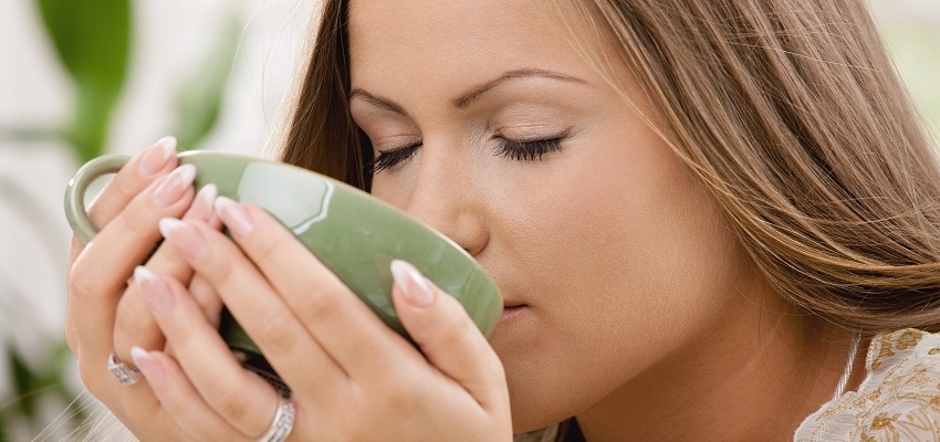 Close em uma mulher tomando chá de uma xícara verde