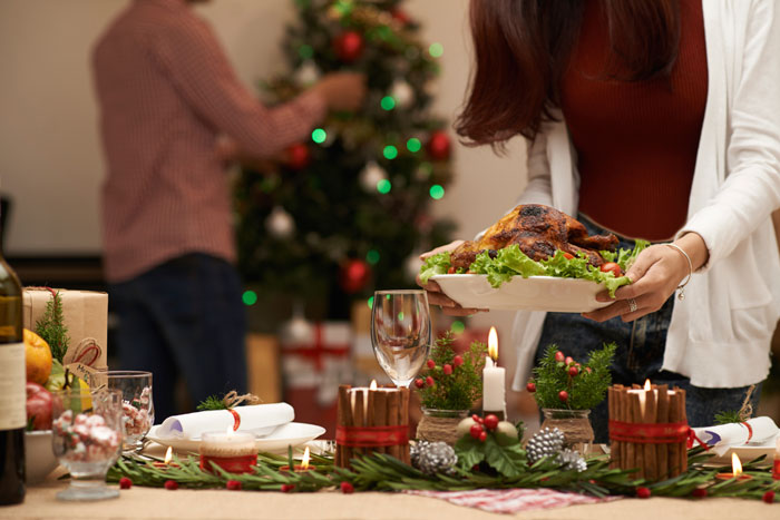 Mulher colocando um prato com peru em uma mesa decorada para a ceia de Natal