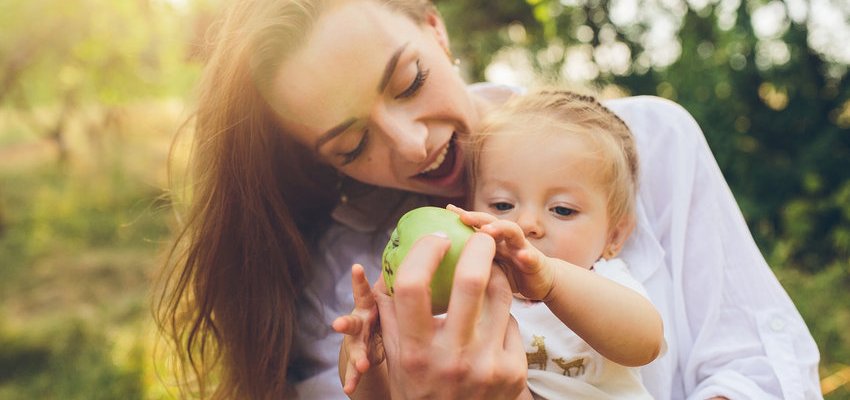 Criança pegando maçã verde da mão da mãe