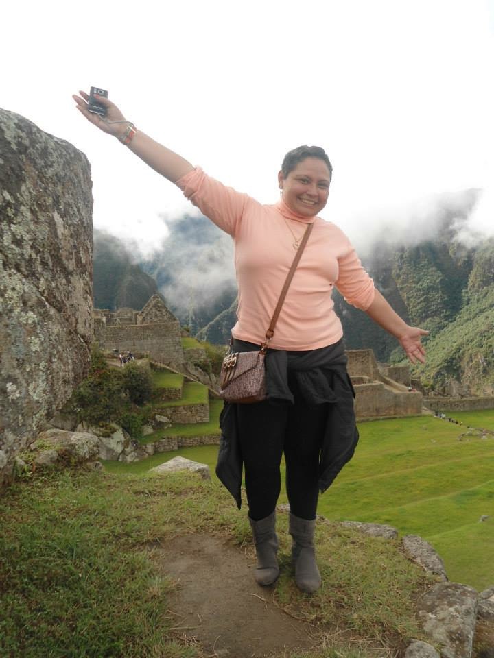 Colaboradora Carol de braos abertos em cima de uma pedra com uma vista cheia de nuvens atrs