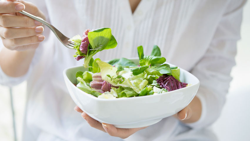Mulher segurando uma vasilha com salada dentro em uma mão e um garfo na outra