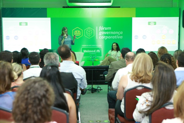 Palestrante no palco com convidada e público sentado assistindo a palestra
