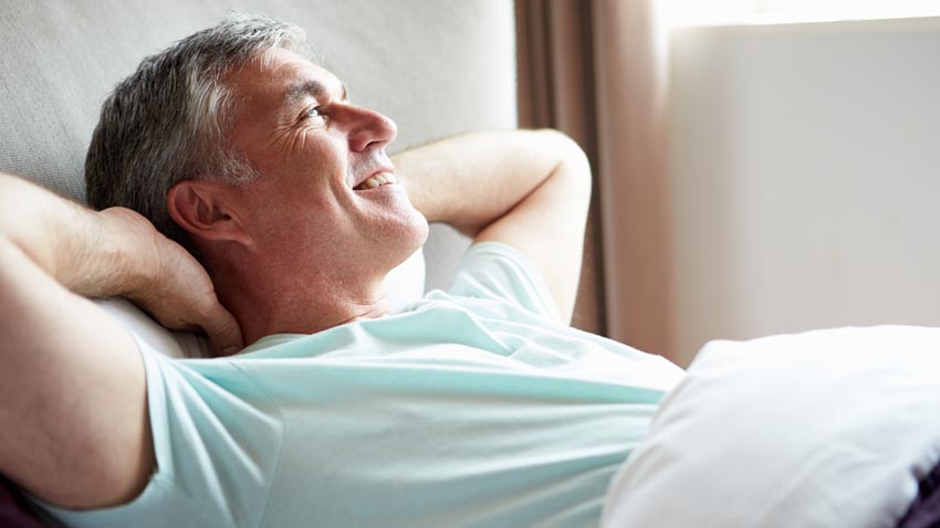 Homem feliz deitado na cama com os braos na cabea