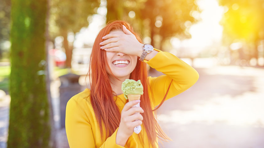 Mulher sorrindo segurando sorvete com uma mo e com a outra tampando os olhos