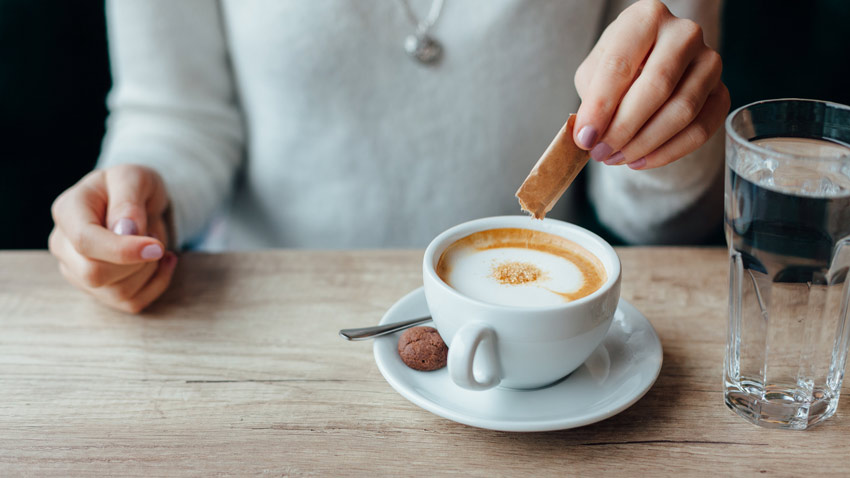 Imagem com foco em uma xcara de caf com um cookie ao lado da xcara e um copo de gua do lado