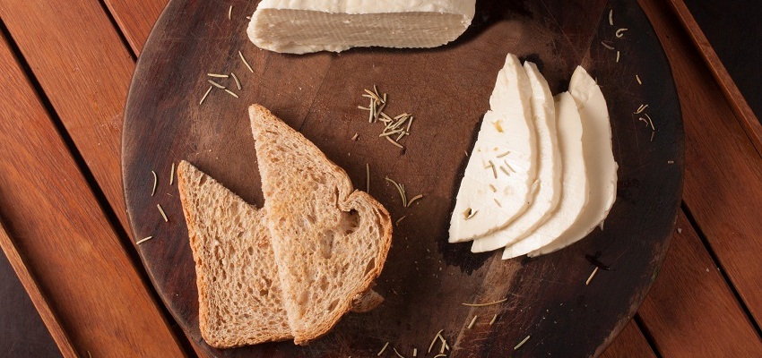 Fatias de pão integral e de queijo minas expostas em uma tábua de madeira
