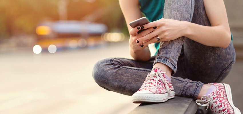 Adolescente sentada perto de uma rua movimentada mexendo no celular