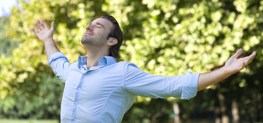 Homem de braos abertos ao ar livre respirando profundamente