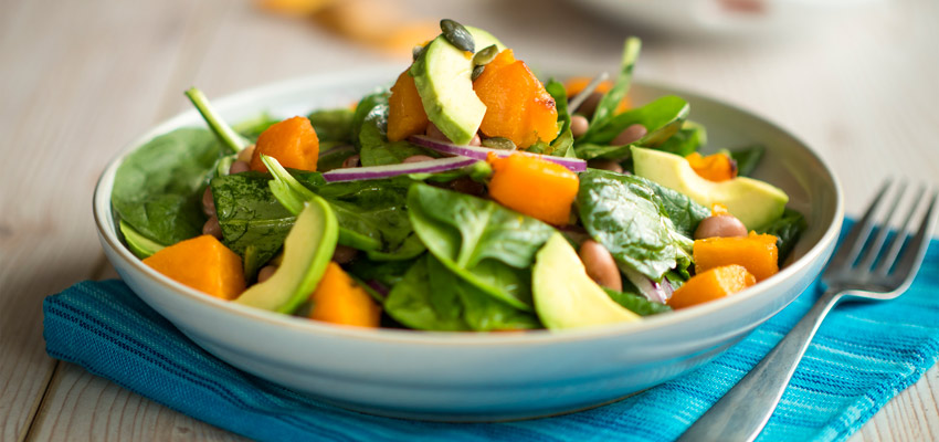 Prato com salada servido em uma mesa de madeira com um garfo ao lado