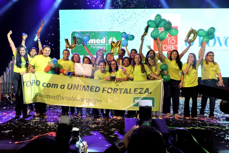 Colaboradores recebendo prmio do GPTW no palco com faixa escrito "Topo com a Unimed Fortaleza"