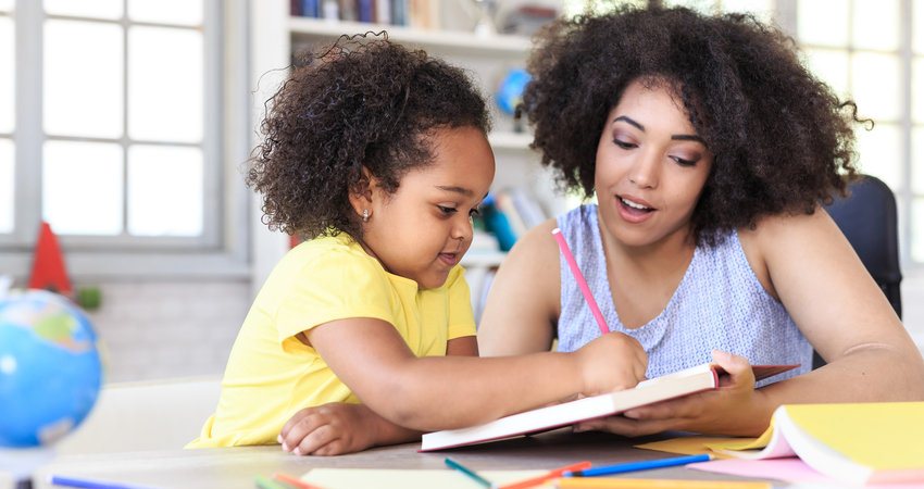 Mãe auxiliando criança com distúrbio de aprendizagem que está escrevendo em um livro