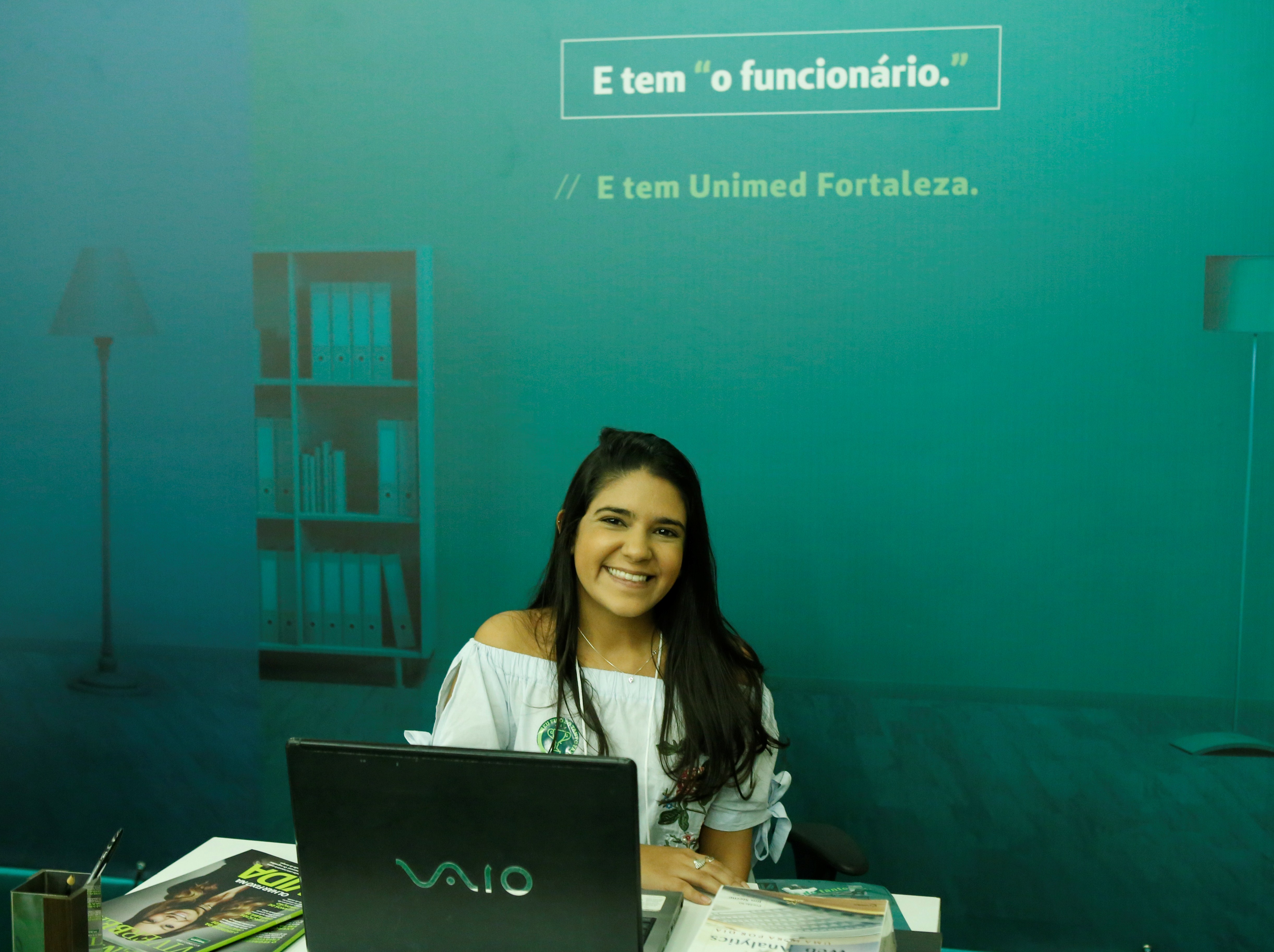 Mulher posa em frente ao banner da campanha corporativa da Unimed Fortaleza.