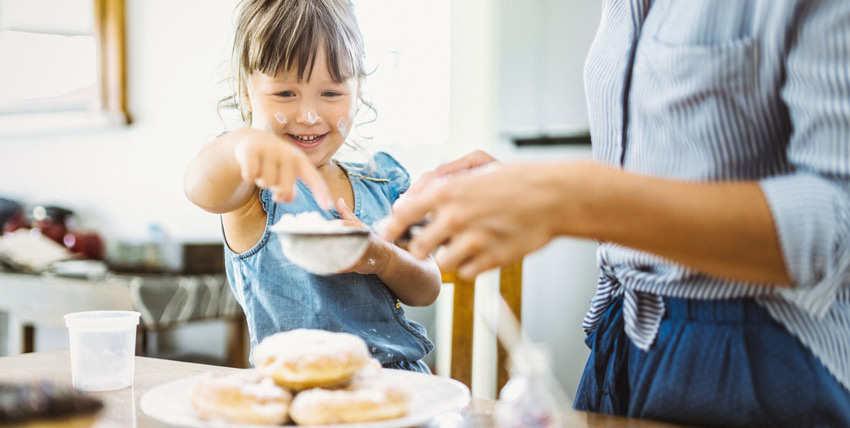 Menina colocando açúcar por cima de rosquinhas ao lado de sua mãe ajudando na reflexão de como reduzir o consumo de açúcar