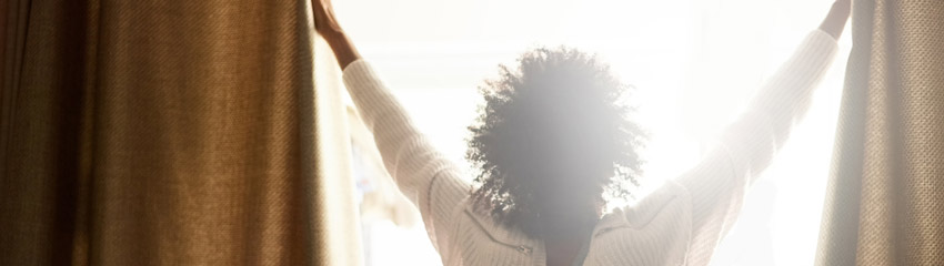 Mulher abrindo as cortinas de uma janela, que tambm ajuda quem tem problemas respiratrios