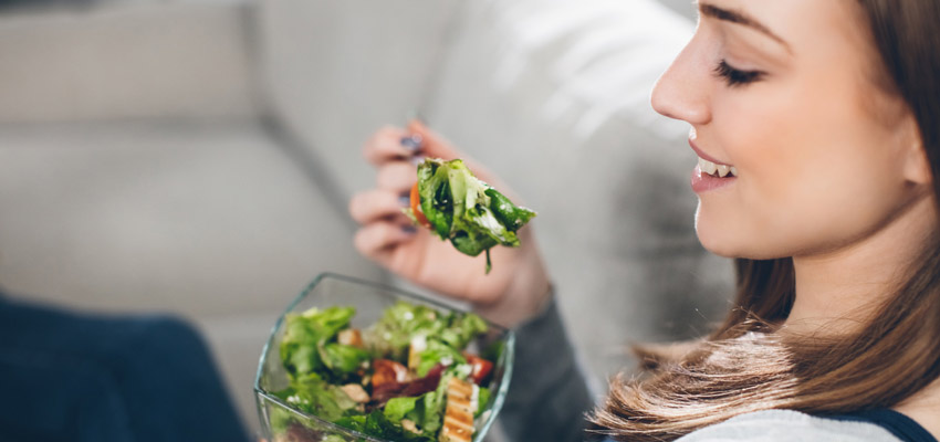 Mulher comendo salada, o que pode ajudar a quem tem compulso alimentar