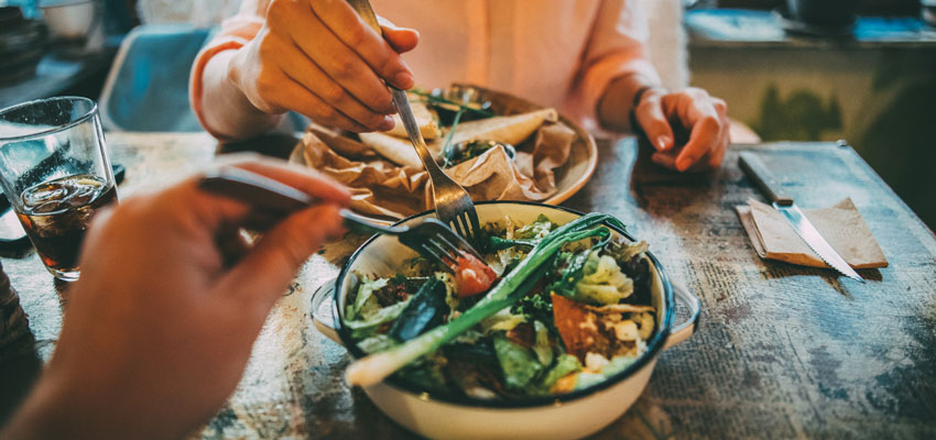 Casal comendo salada em uma mesa provando que no  preciso ter mau humor na dieta