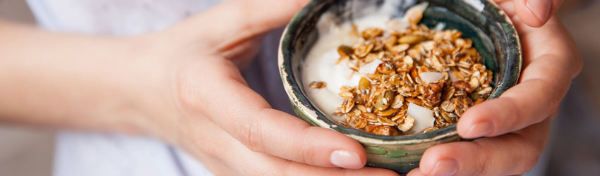 Mos de mulher segurando um pote com iogurte natural e granola, um exemplo de comida saudvel que exemplifica que no  caro ser saudvel