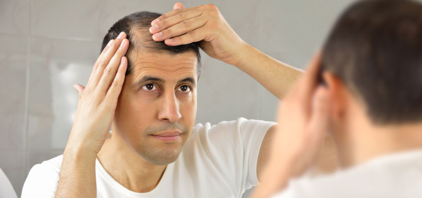 Homem olhando para seu cabelo no espelho provavelmente se perguntando como prevenir a queda de cabelo