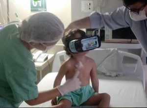 Giovanna sentada na cama do hospital, experimentando o culos de Realidade Virtual oferecido pela Unimed Fortaleza