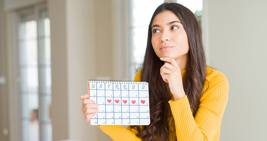 Mulher pensativa segurando calendário do seu período fértil